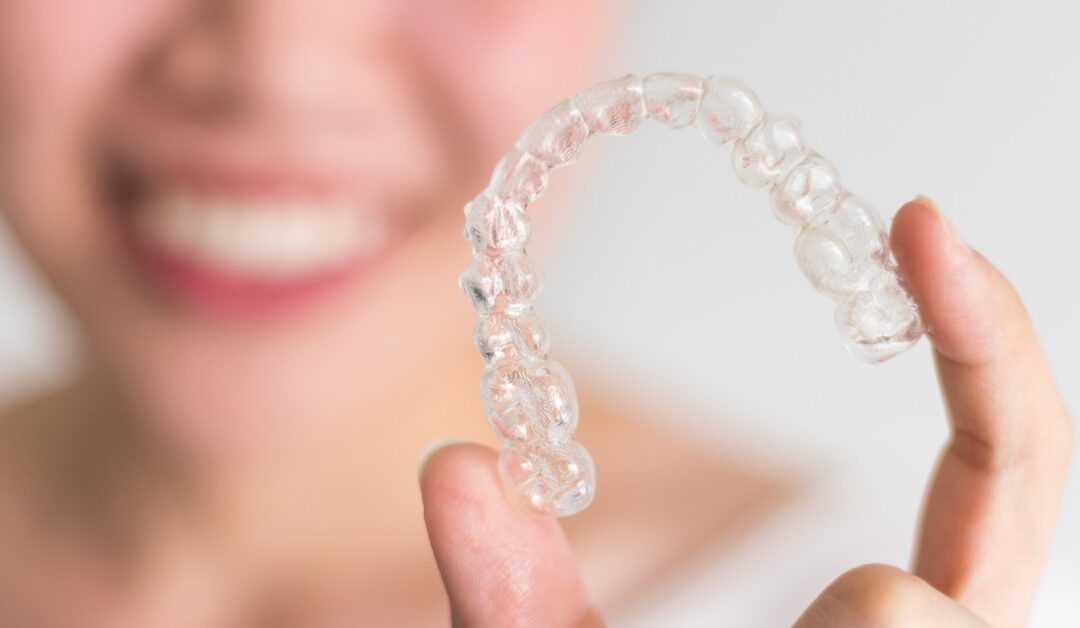 A person is holding a clear plastic mold of their teeth between their fingers, and their face is blurred in the background.