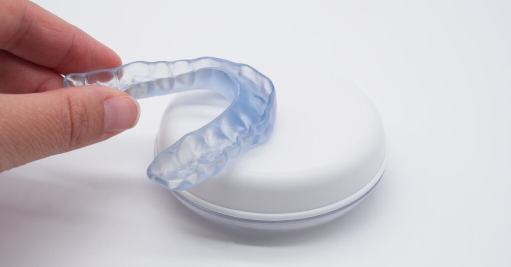 A person places a transparent night guard onto the top of a white case. A white surface fills the background.