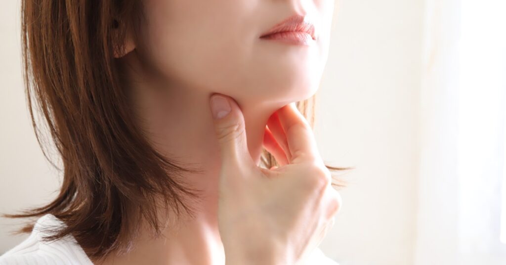 A woman with short hair tilts up her head. She pinches her neck just below her jaw to alleviate pain.