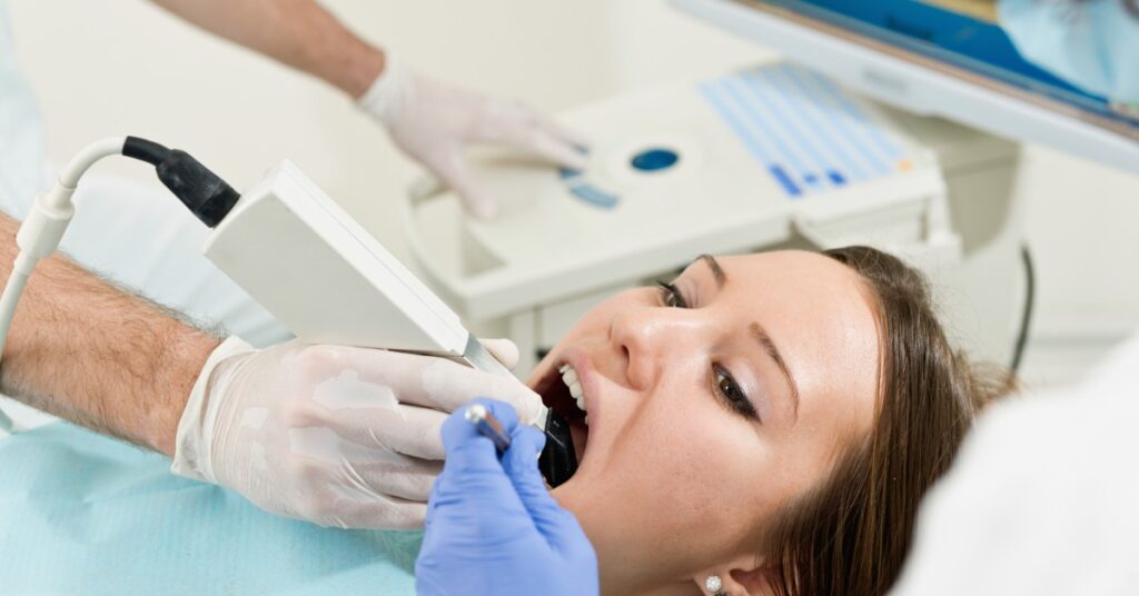 A woman wears a blue bib while lying on a table in a dentist's office The dentist adds a ceramic inlay to the tooth.
