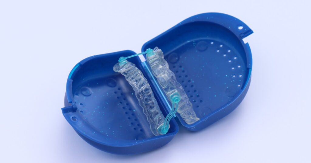 A close-up of a sleep apnea oral appliance that's positioned in an open blue mouthguard case. The background is a light blue.