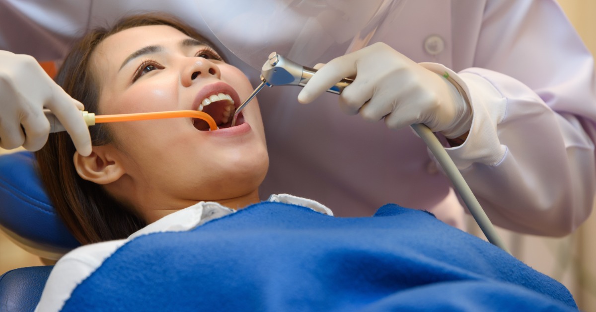 A dentist holds an air water syringe in a patient's mouth. The patient wears a blue bib on their chest.