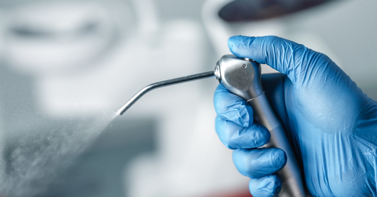 An extreme close-up of a hand wearing a blue glove pushing down on a air water syringe and releasing water into the air.
