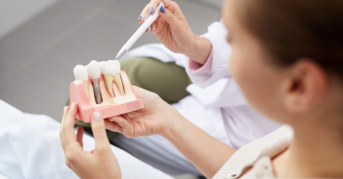 A patient is holding a tooth model during a dental consultation. The dentist uses a pen and points to the model.