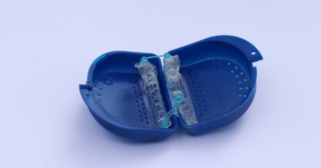 A clear oral appliance with blue connectors is resting inside of an open blue plastic case on a light surface.